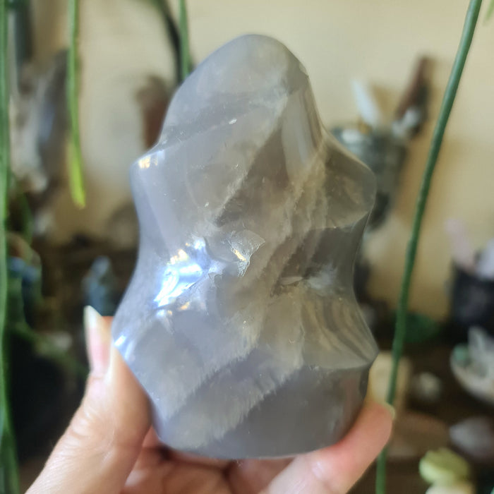 A polished Blue Rose Quartz crystal with a smooth, solid gray appearance, held in a person's hand.