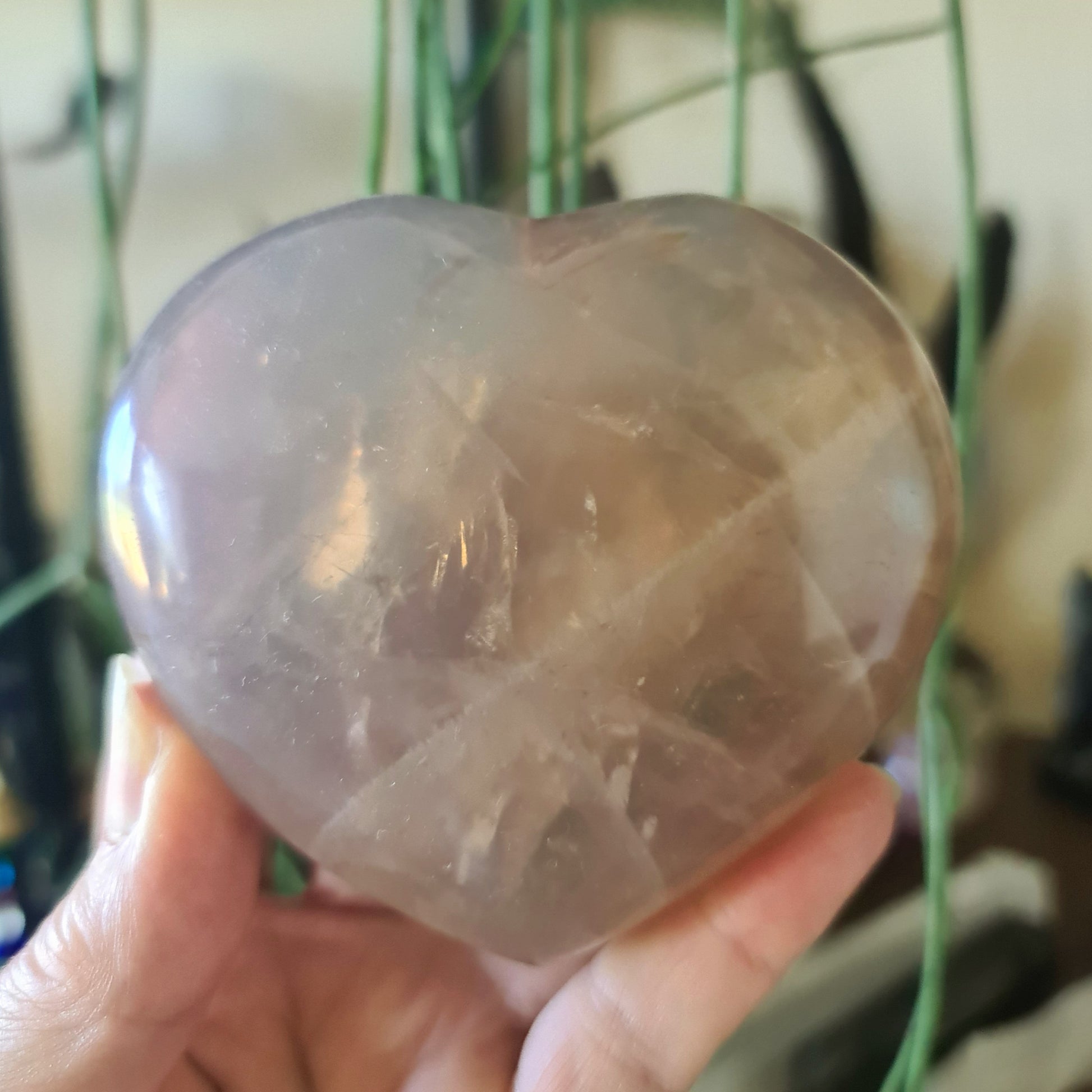 A heart-shaped Blue Rose Quartz crystal being held in a person's hand.