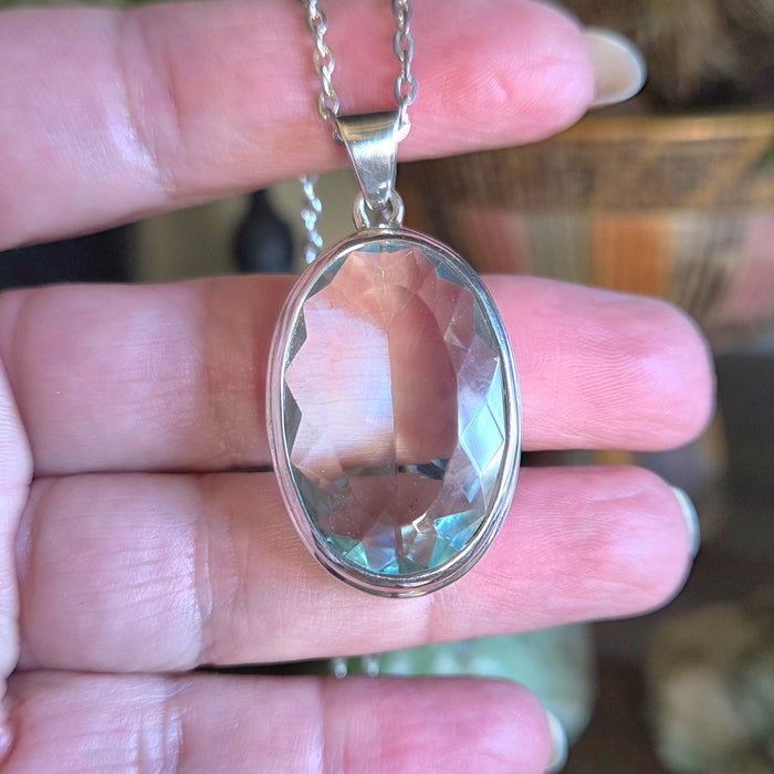 Silver pendant with a clear blue stone held between fingers