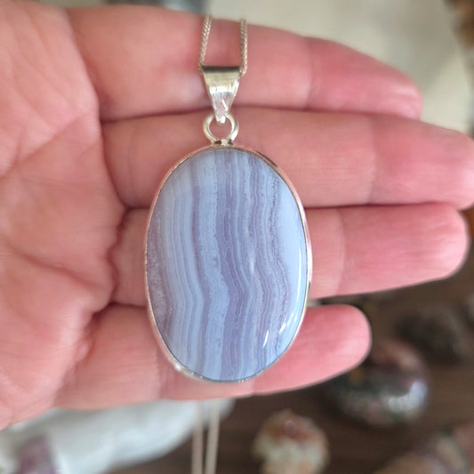Blue stone pendant on a silver chain held in a hand
