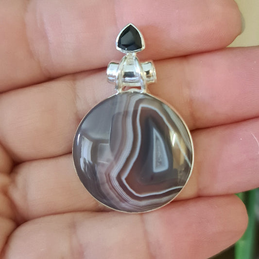 A teardrop-shaped pendant with a black onyx border and a central botswana agate stone, set in a sterling silver setting.