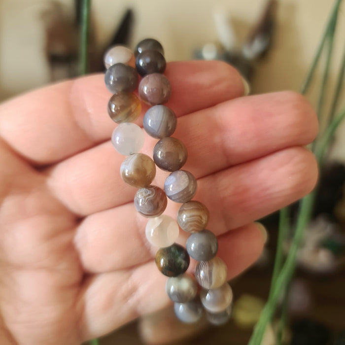 A hand holding a bracelet made of round Botswana agate stones.
