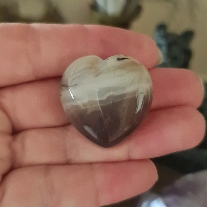 A hand holding a heart-shaped Botswana Agate gemstone.