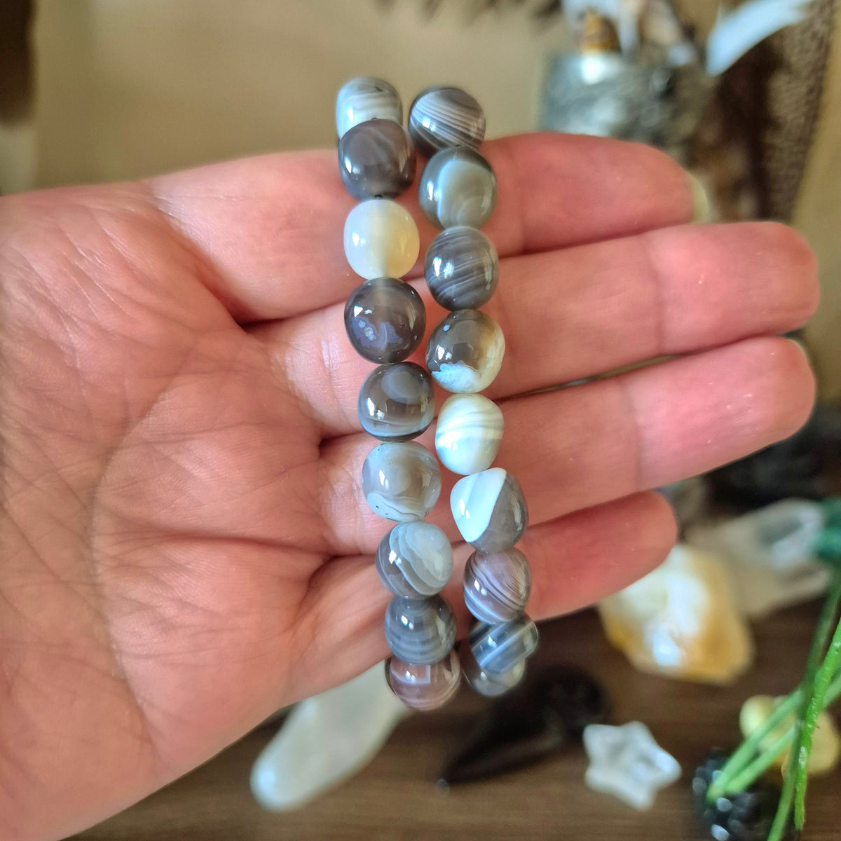 A hand holding a Botswana Agate Pebble Bracelet with a mix of gray, brown, and pink colors.