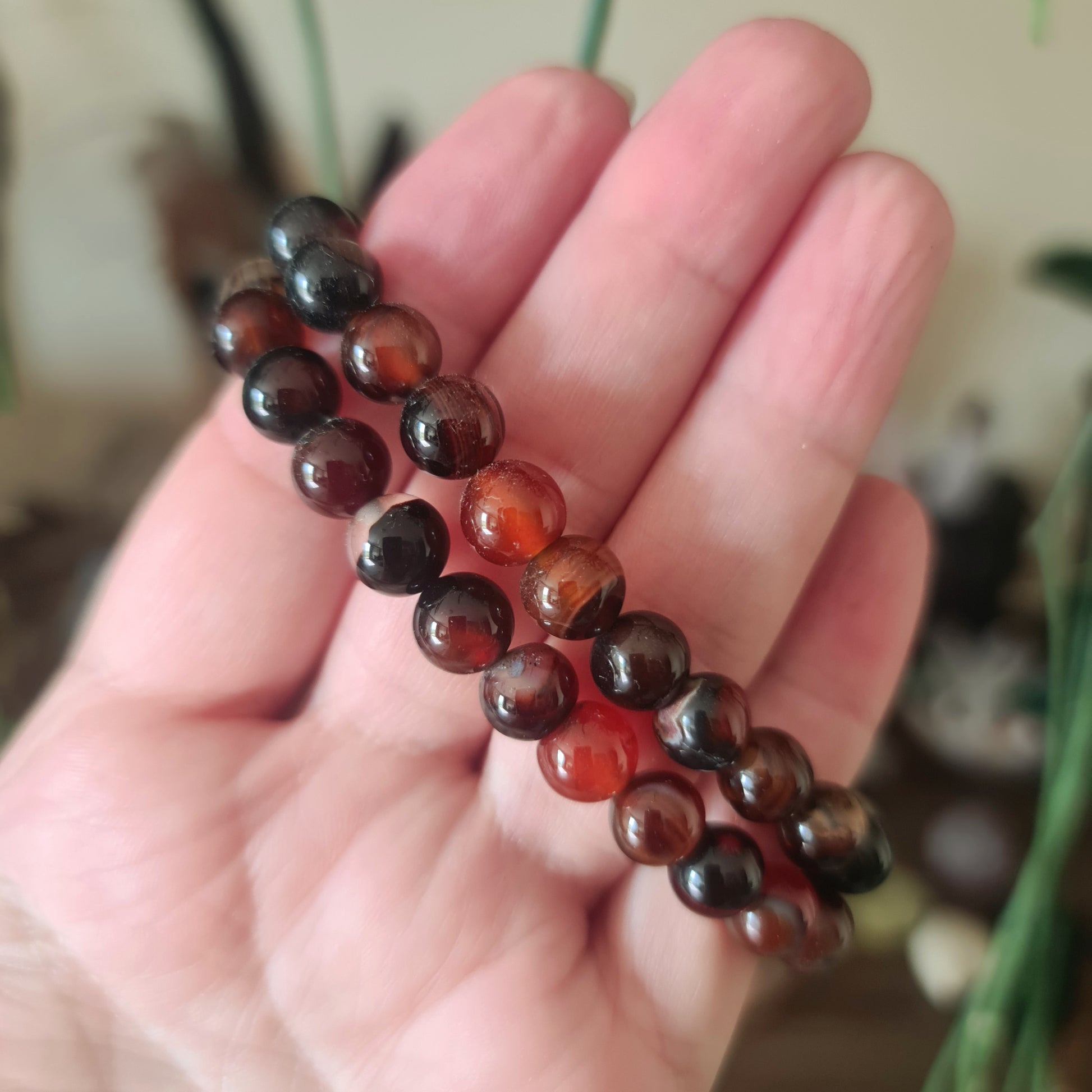 A hand holding a brown agate bracelet with a series of irregularly shaped stones strung on a beaded chain.
