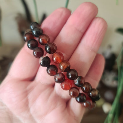 A hand holding a brown agate bracelet with a series of irregularly shaped stones strung on a beaded chain.