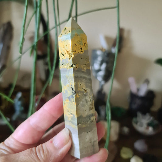 A polished Bumblebee Jasper crystal point being held in a person's hand.