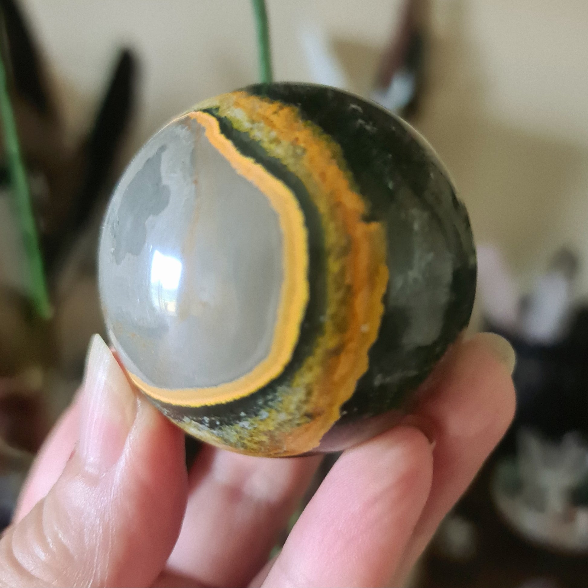 A hand holding a Bumblebee Jasper sphere with yellow and green color patterns.