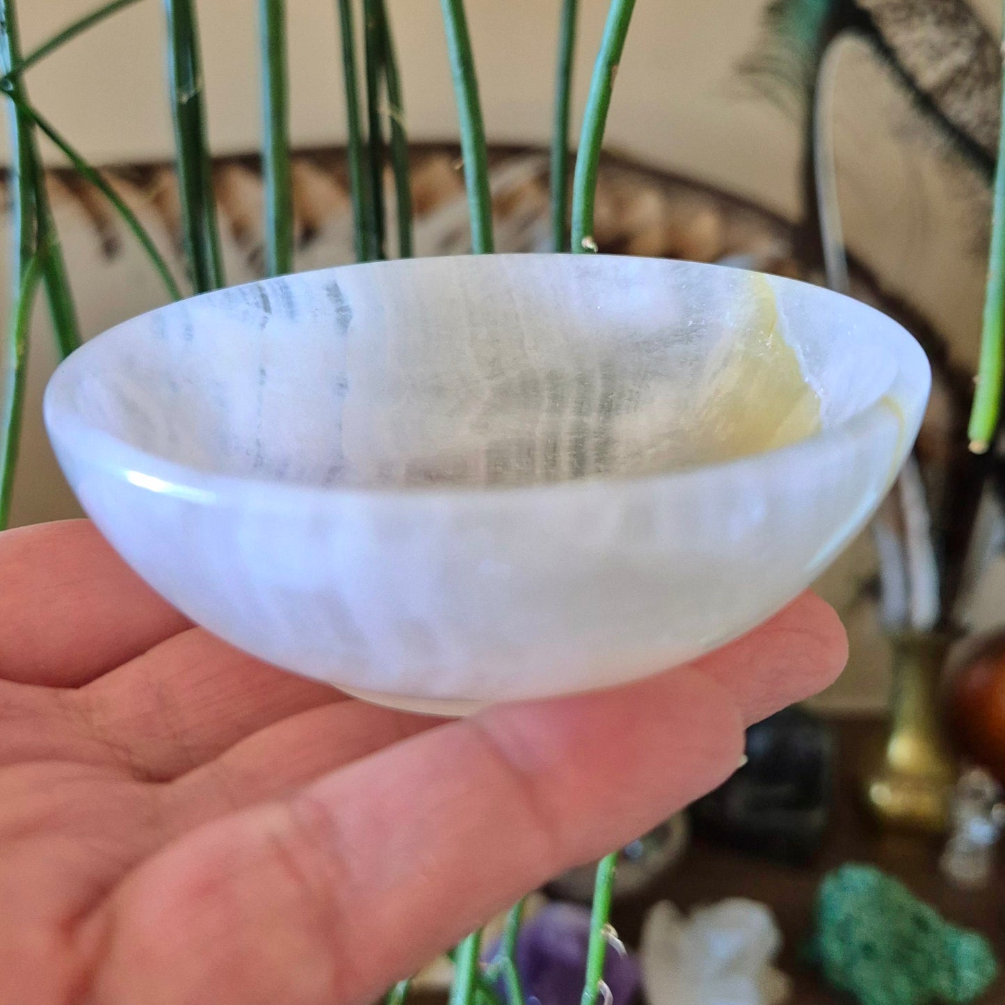 This image features a delicate and intricately crafted Calcite Bowl. The bowl is held in a person's hand, providing a clear view of its smooth, polished surface with a subtle iridescence that suggests its calcite composition.
