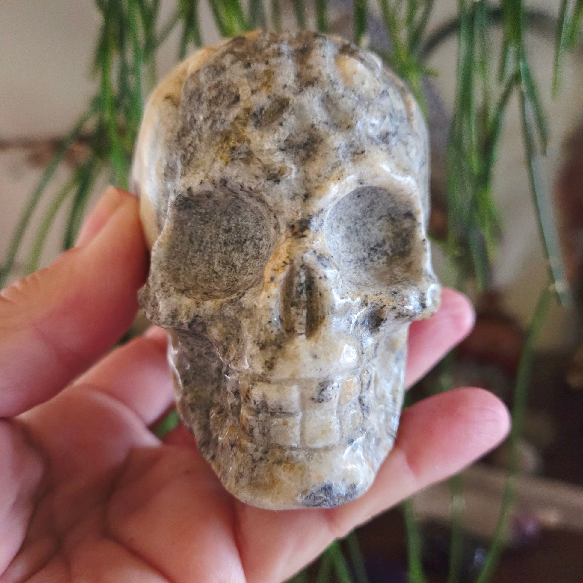 A hand holding a natural stone skull carving with gray and beige colors.
