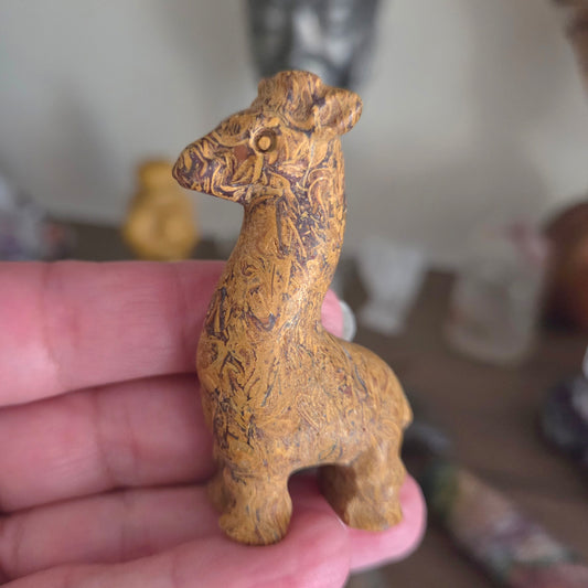 A small carved animal figurine with a textured, swirling wood-like pattern in warm brown and tan tones, held in a person's hand against a blurred indoor background.