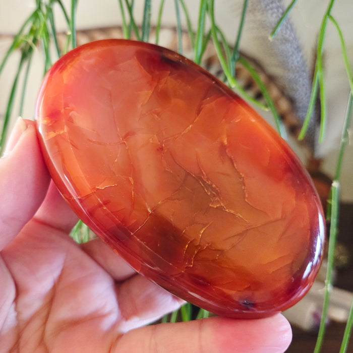 A hand holding a polished red carnelian stone bowl with a smooth surface.