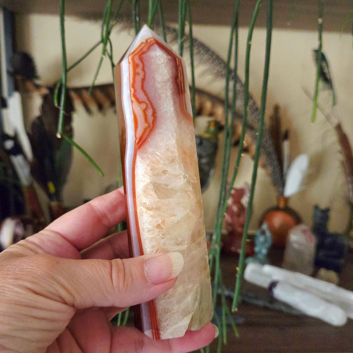 A hand holding a carnelian quartz obelisk with a background of various items.