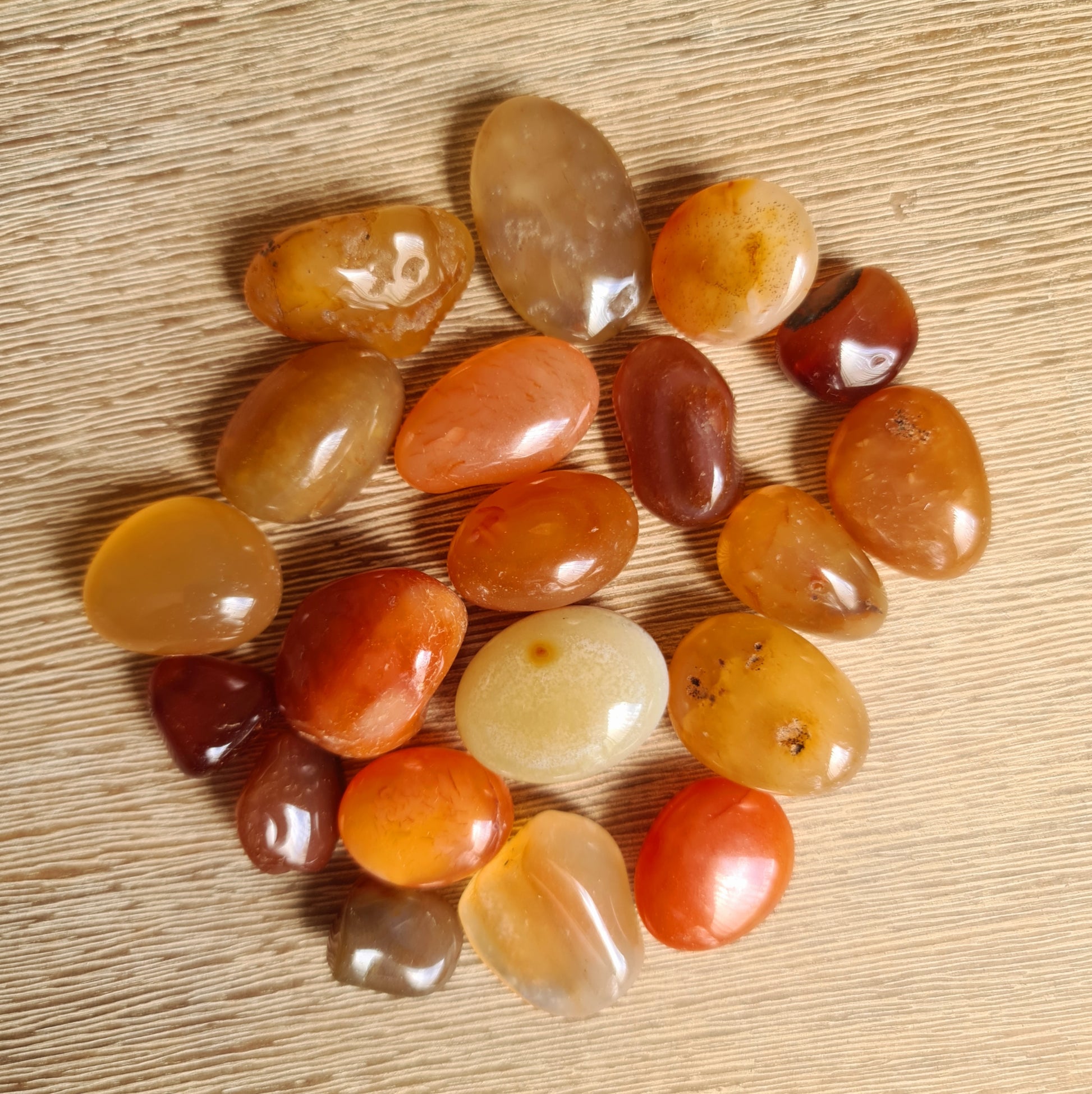A collection of Carnelian tumble stones displayed on a wooden surface.