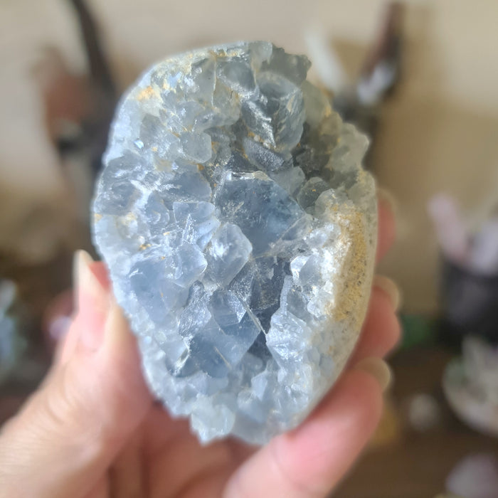 A large blue Celestite crystal cluster held in a person's hand.