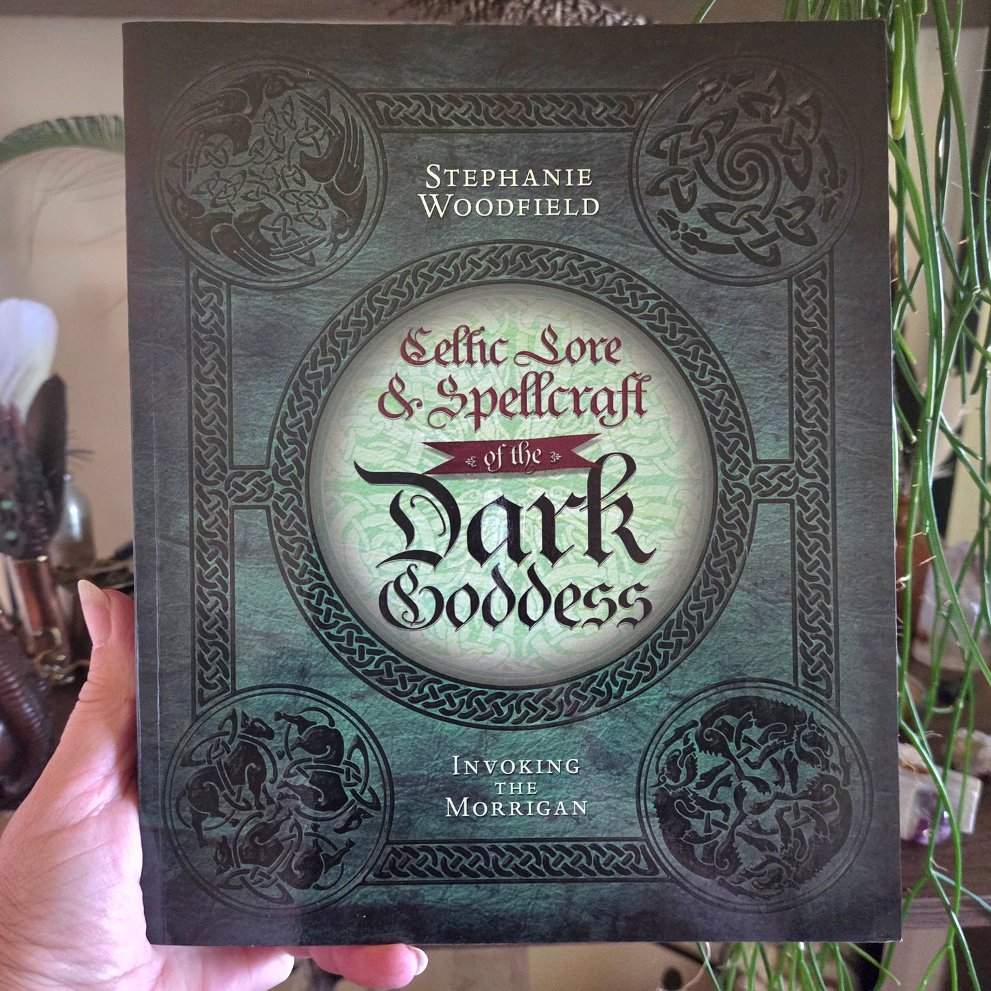 Book titled 'Celtic Lore & Spellcraft of the Dark Goddess' held by a person with decorative background