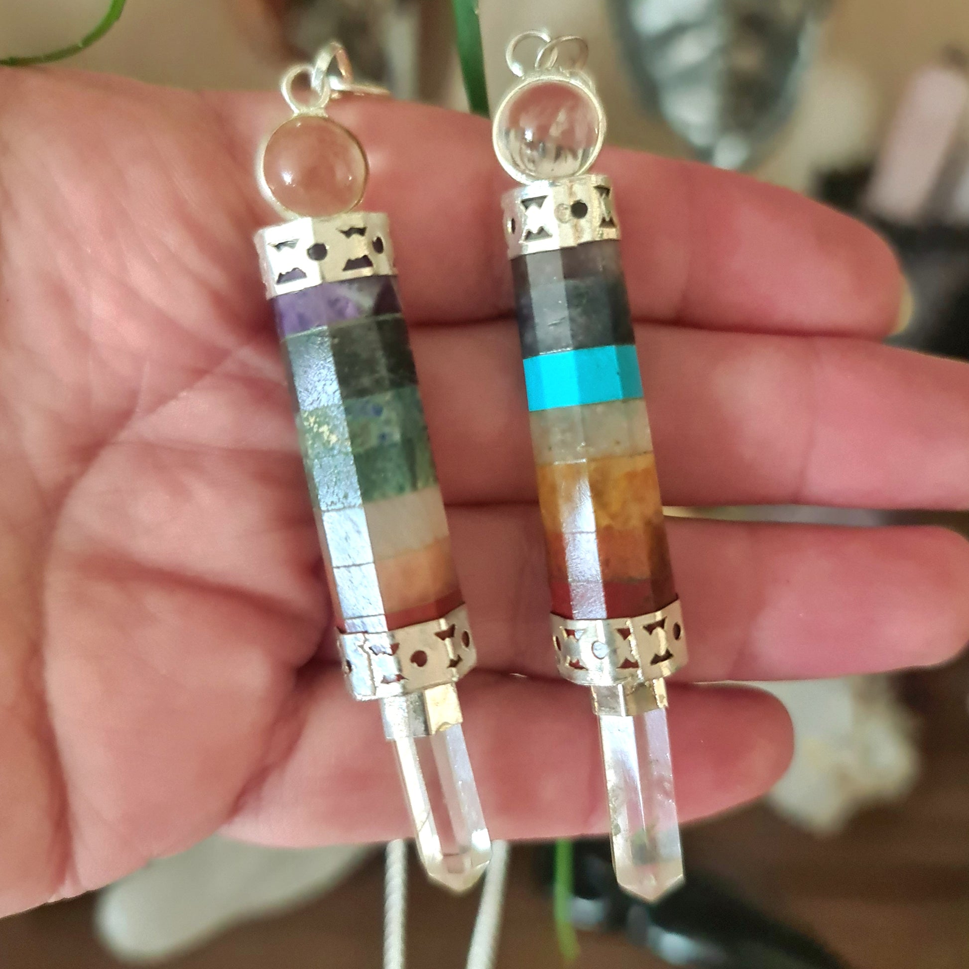 Two chakra pendulum wands with beaded details and crystal ends, held in a person's hand.