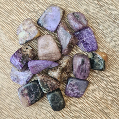 A collection of polished Charoite tumbled stones displayed on a wooden surface.