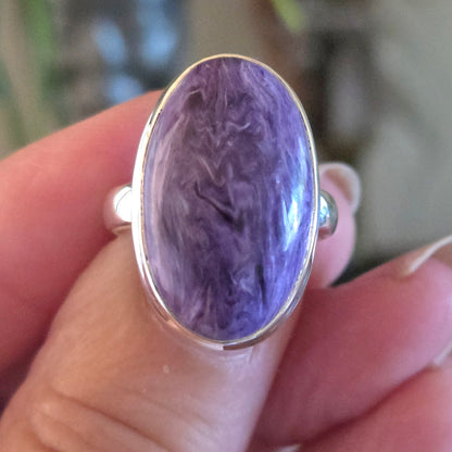 Ring with a purple stone held in a hand against a blurred natural background