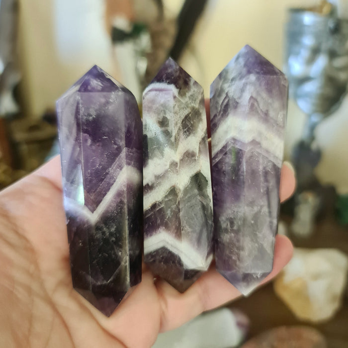 Three polished Chevron Amethyst crystals with white quartz patterns, held in a person's hand.