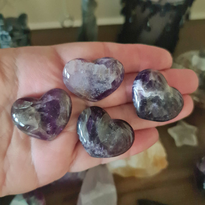 A hand holding a polished heart-shaped Chevron Amethyst crystal.