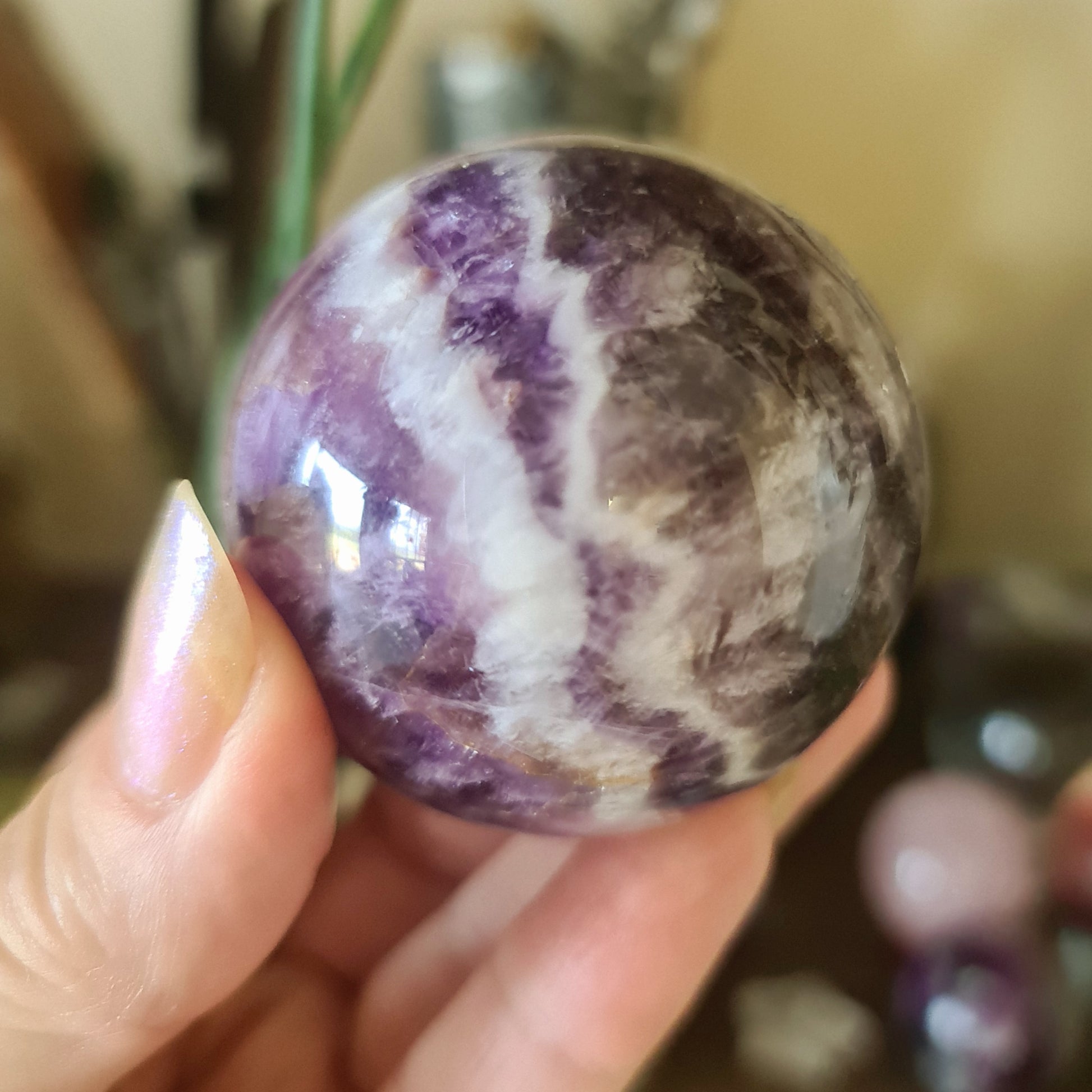 A purple and white striped Chevron Amethyst sphere held in a person's hand.