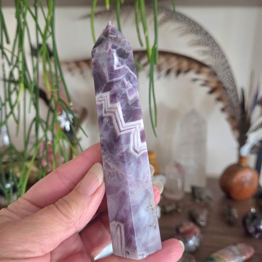 Hand holding a purple crystal with geometric patterns against a bohemian decor background