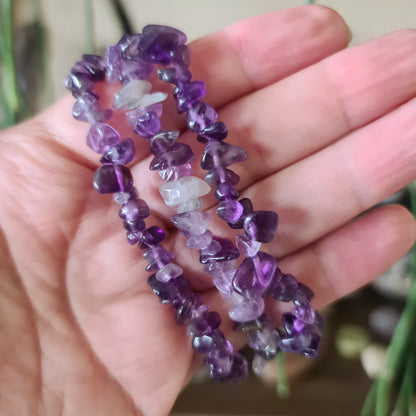 A hand holding a chip bracelet made of purple crystals.