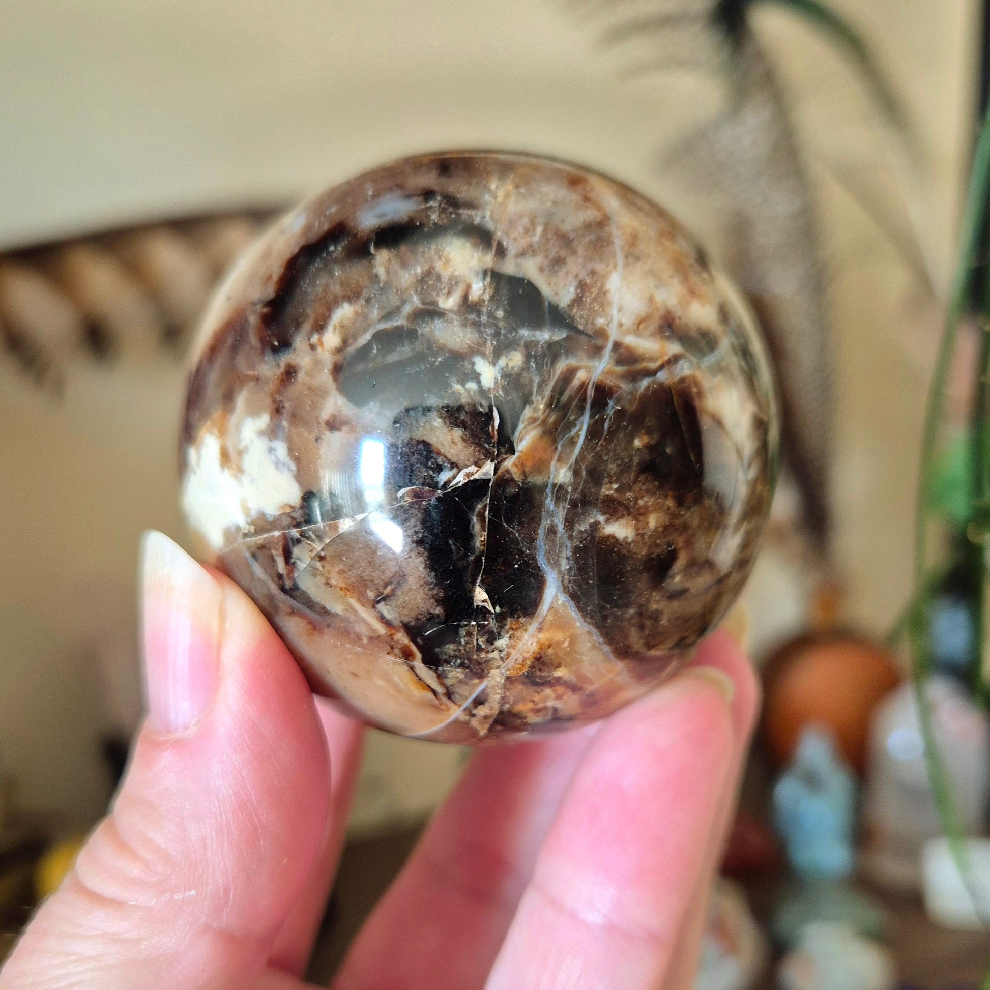 A polished chocolate calcite sphere held in a person's hand, with a blurred background.