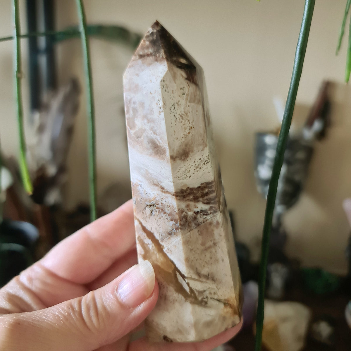 A hand holding a chocolate calcite tower crystal with a brown and white patterned surface.