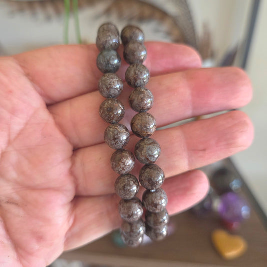 Hand holding a bracelet with brown beads against a blurred background