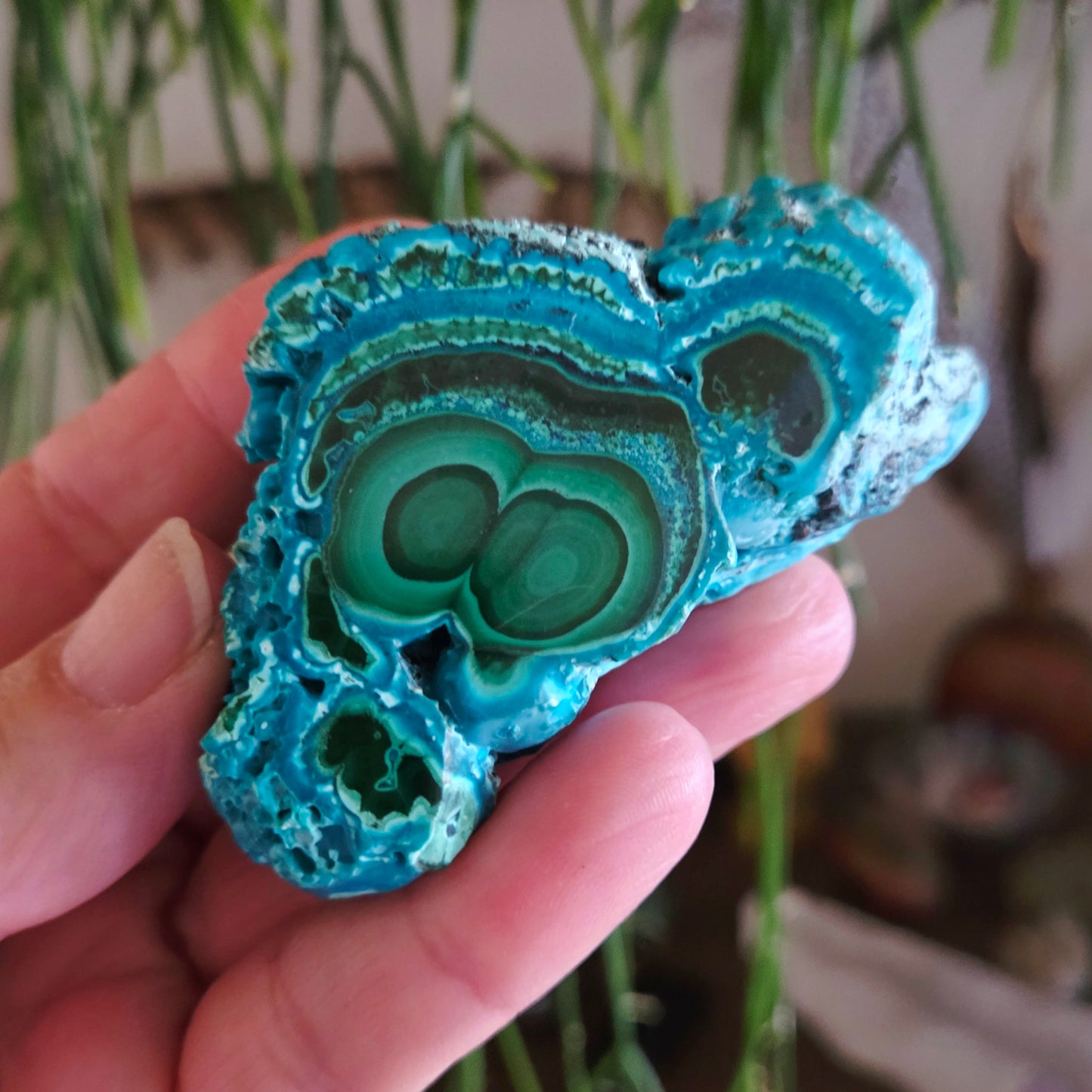 A freeform Chrysocolla gemstone held in a person's hand, with a vibrant blue color and intricate patterns.