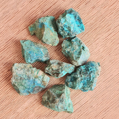 A collection of polished chrysocolla stones with a blue to green gradient, placed on a wooden surface.