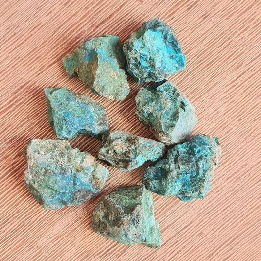 A collection of polished chrysocolla stones with a blue to green gradient, placed on a wooden surface.