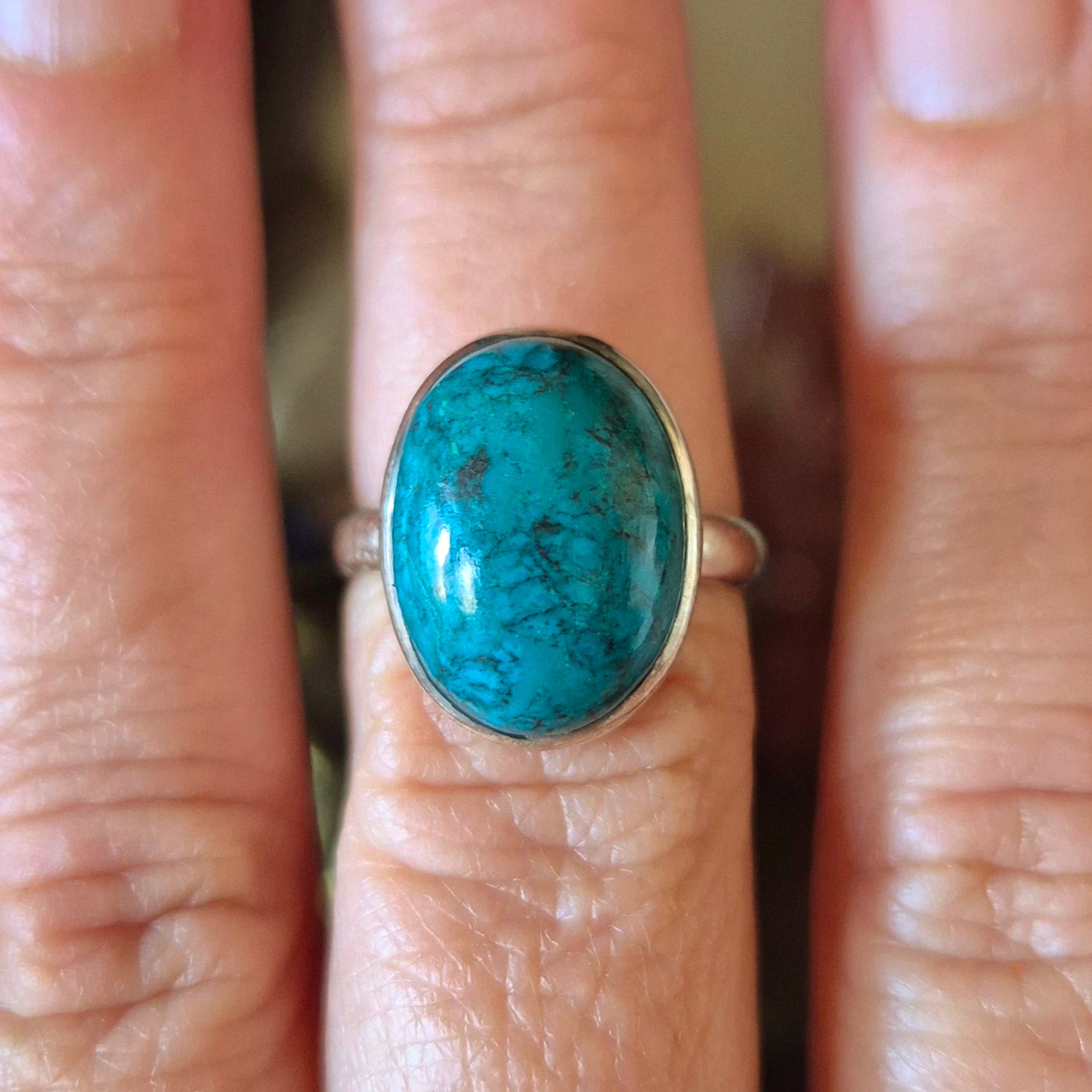 A hand holding a Chrysocolla ring with a blue and green marbled appearance, size 7.