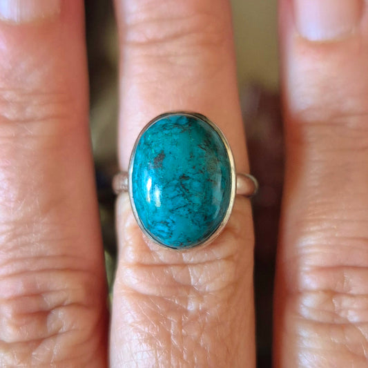A hand holding a Chrysocolla ring with a blue and green marbled appearance, size 7.