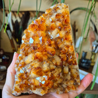 A hand holding a polished citrine crystal cluster with a faceted surface.