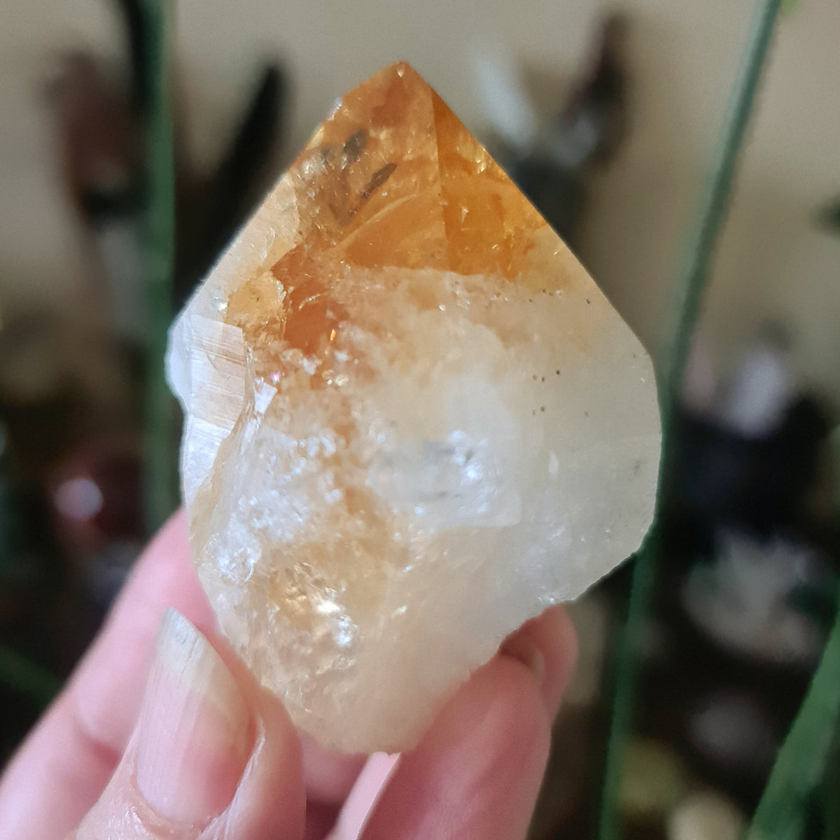 A large citrine crystal point held in a person's hand, with a warm orange hue and a polished surface.