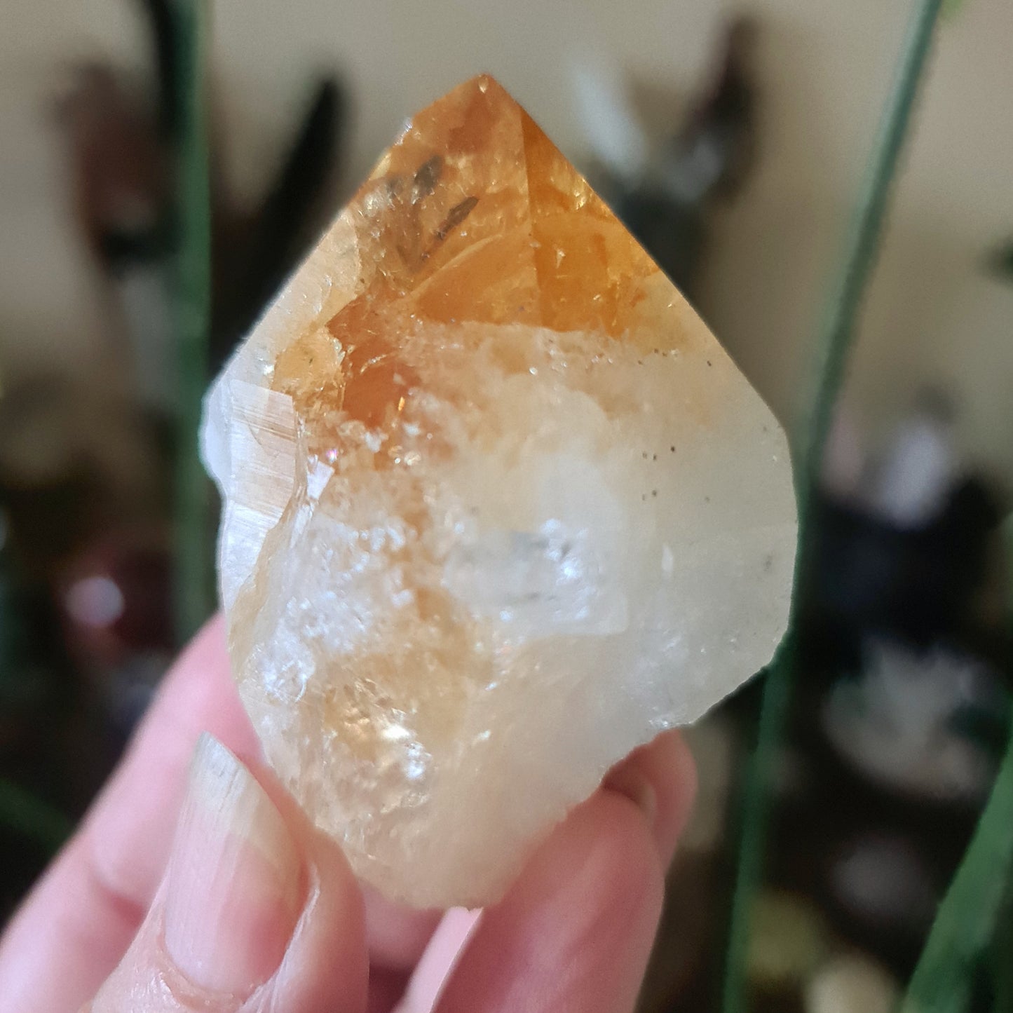 A large citrine crystal point held in a person's hand, with a warm orange hue and a polished surface.