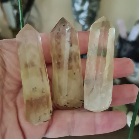 Three polished yellow citrine crystal points, each with a different shape, held in a person's hand.