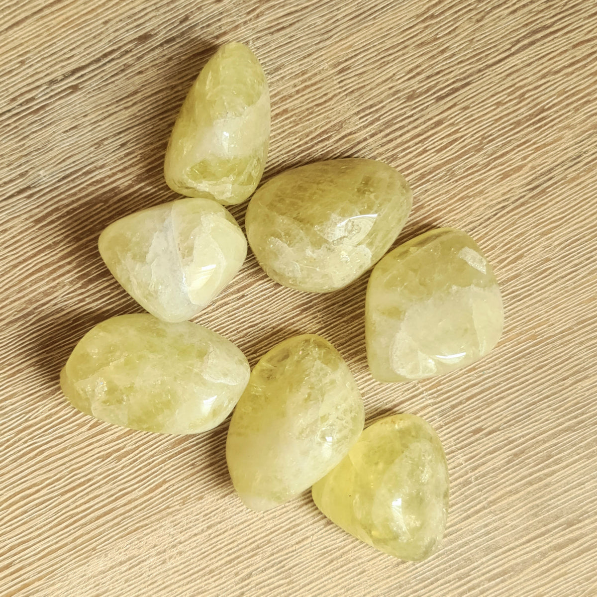 A collection of polished green Citrine tumble stones on a wooden surface.