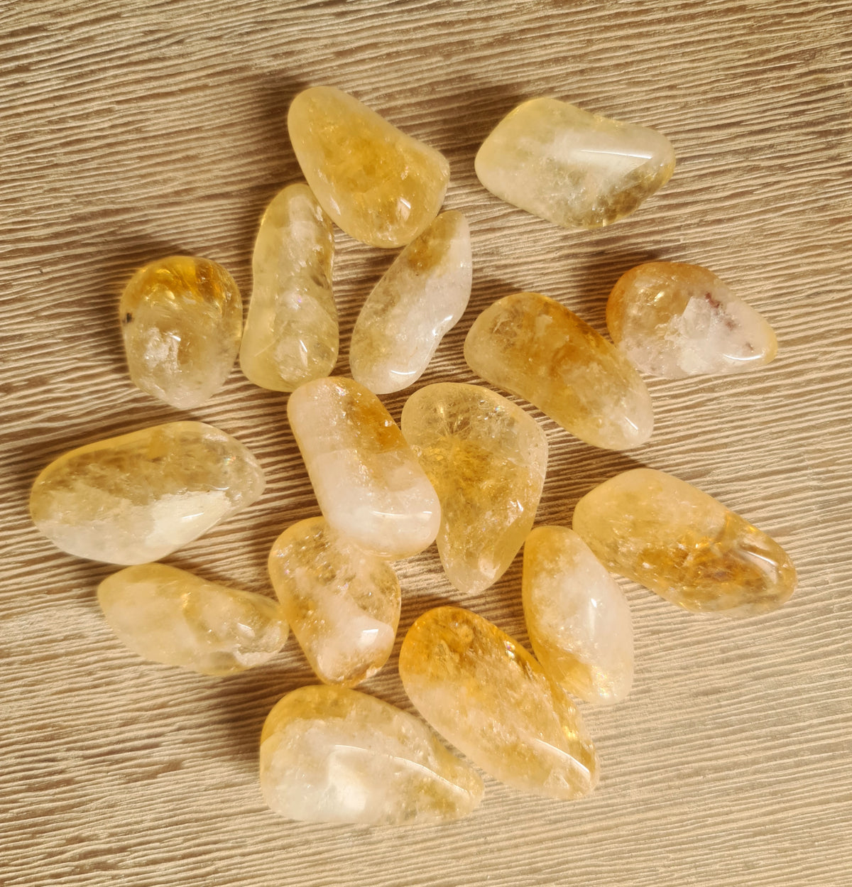 A collection of polished citrine tumble stones displayed on a wooden surface.