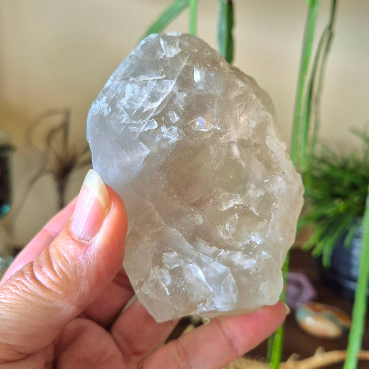 A hand holding a clear, raw, freeform-shaped clear calcite crystal.