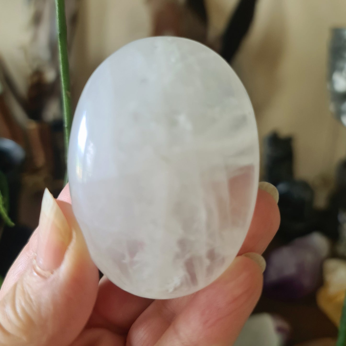 A polished, white egg-shaped calcite crystal being held in a person's hand.