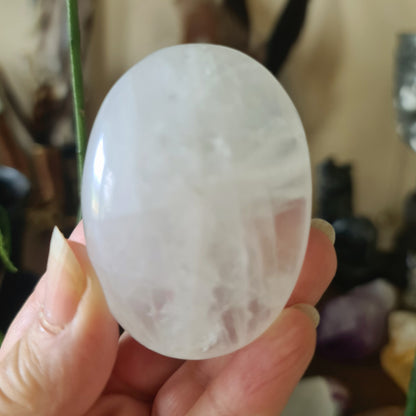 A polished, white egg-shaped calcite crystal being held in a person's hand.