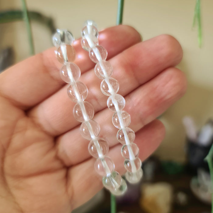 A hand holding a clear quartz crystal bracelet with a series of round, transparent beads.