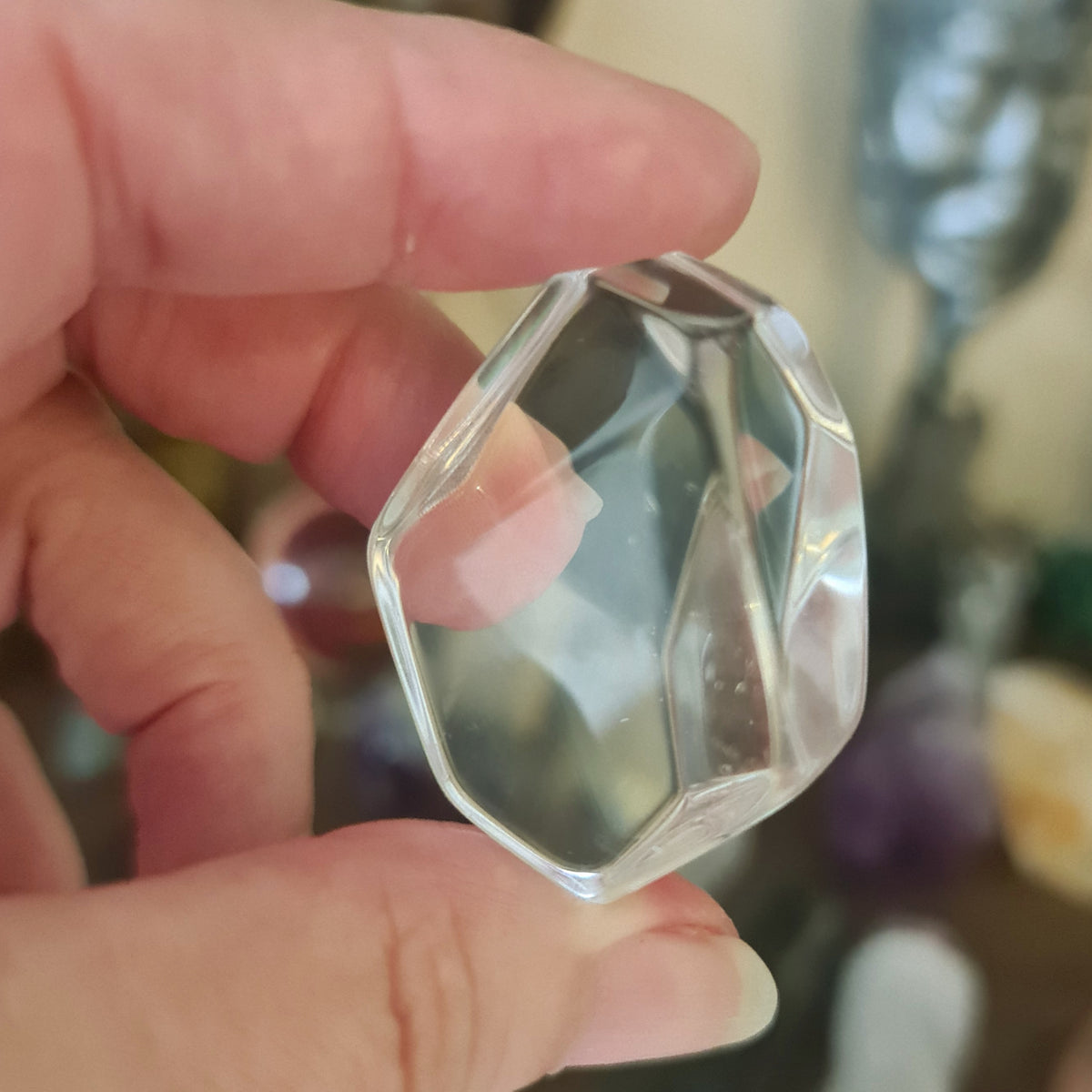 A polished, clear quartz crystal held in a person's hand, with a blurred background suggesting indoor setting