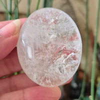 A clear quartz palm stone held in a hand, with a blurred background.
