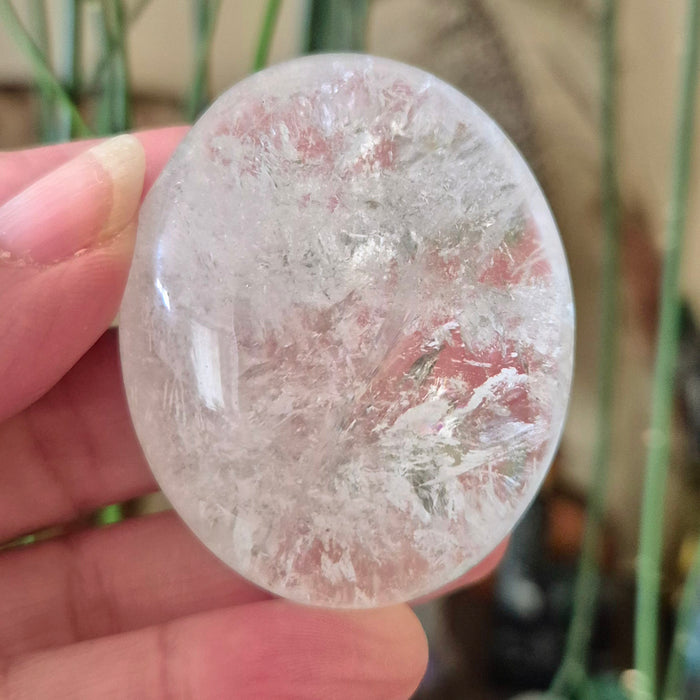 A clear quartz palm stone held in a hand, with a blurred background.