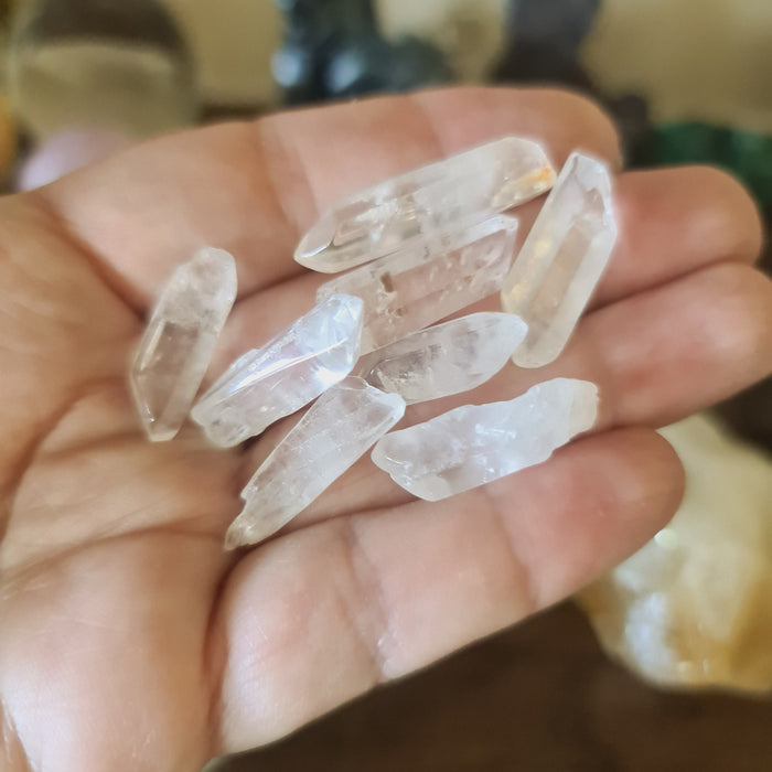 A hand holding several clear quartz crystal points.